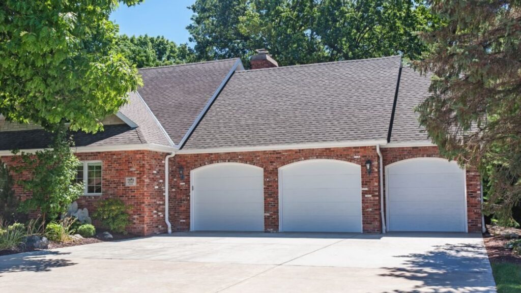 A Large Brick House With Three White Garage Doors.