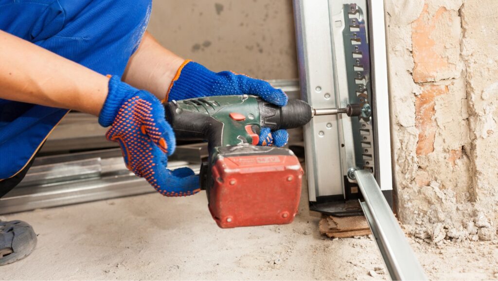 A Technician Uses a Power Drill to Tighten a Garage Door Track.