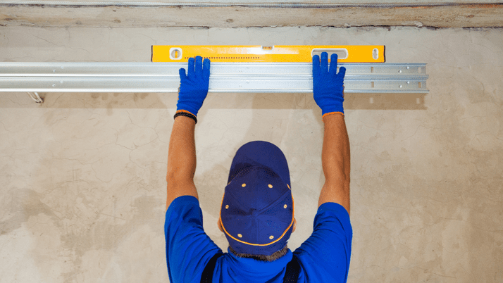 A garage door technician measures the level of a garage door track.