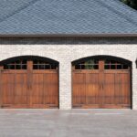 A large brick house with two beautiful wooden garage doors.