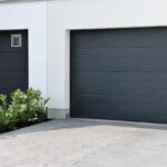 A modern, black garage door on a white house..