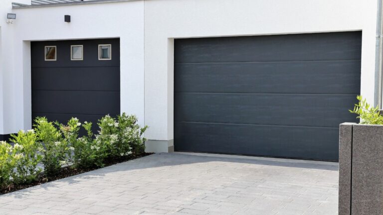 A modern, black garage door on a white house..