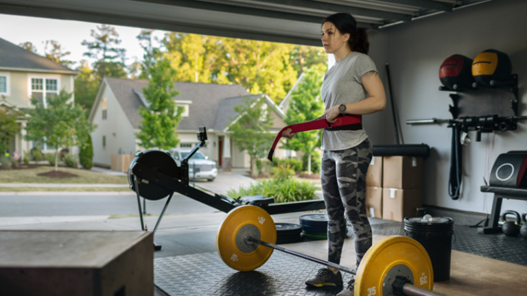 A Woman in Her Garage Home Gym Puts On A Weightlifting Belt