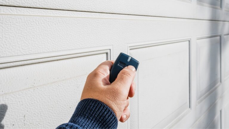 A hand holding an older style garage door opener in front of a garage door.
