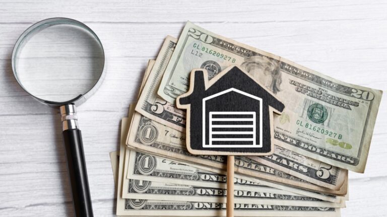 A stack of money next to a magnifying glass and a small wooden house with a garage.