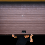 A man manually lifts his home’s garage door and peeks underneath.
