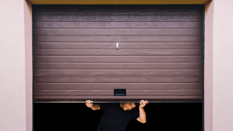 A man manually lifts his home’s garage door and peeks underneath.