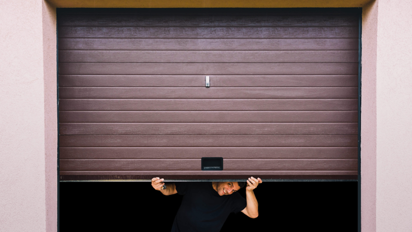 A man manually lifts his home’s garage door and peeks underneath.