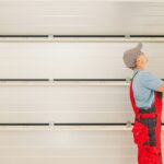 A garage technician uses a long tool to adjust the garage door.