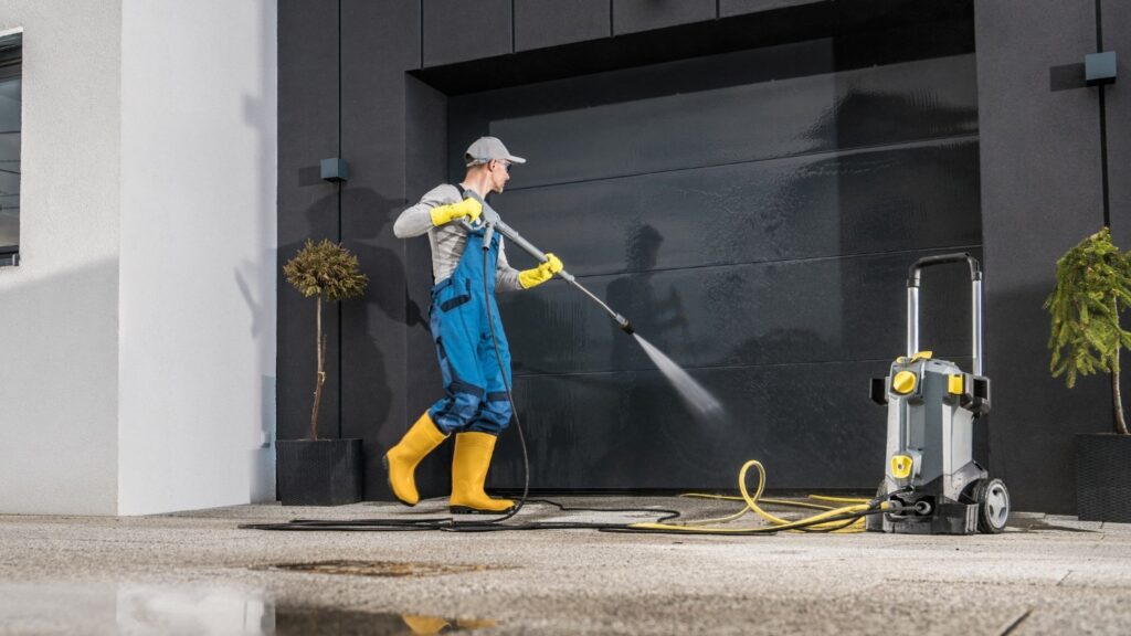 A man in rubber gloves and boots cleans the exterior of a garage door.