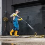 A man in rubber gloves and boots cleans the exterior of a garage door.