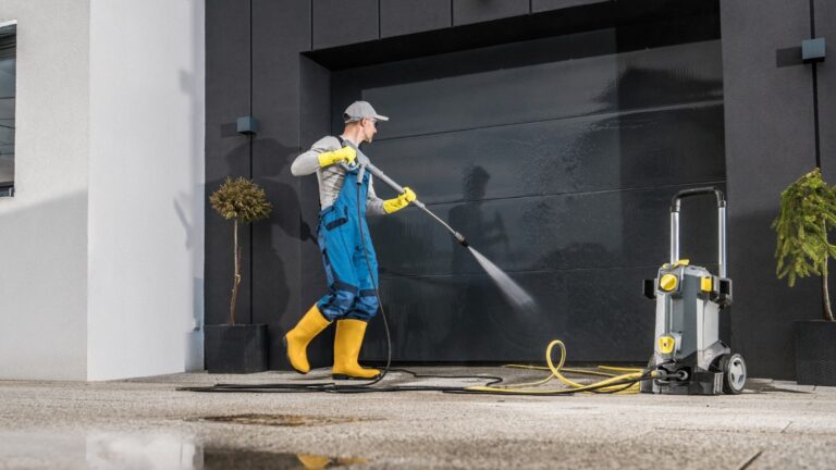 A man in rubber gloves and boots cleans the exterior of a garage door.