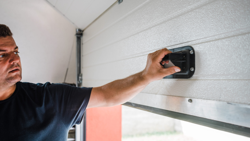 A man pulls up on the interior handle of a garage door.
