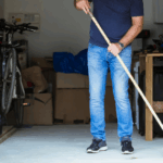 A man sweeps his garage with a push broom to clean it.