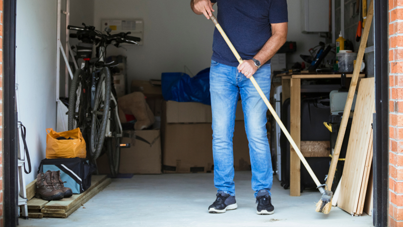 A man sweeps his garage with a push broom to clean it.