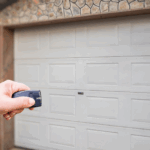 A person holds a garage door opener in front of theri garage door.