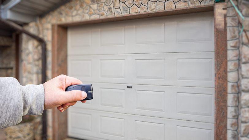 A person holds a garage door opener in front of theri garage door.
