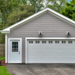 A detached two car garage with a driveway next to a lush green lawn.