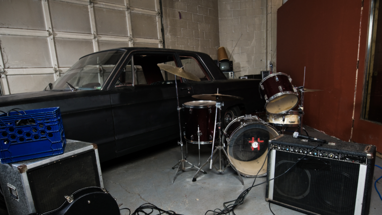 A garage interior with a car and band equipment, including a drum set and amplifiers.