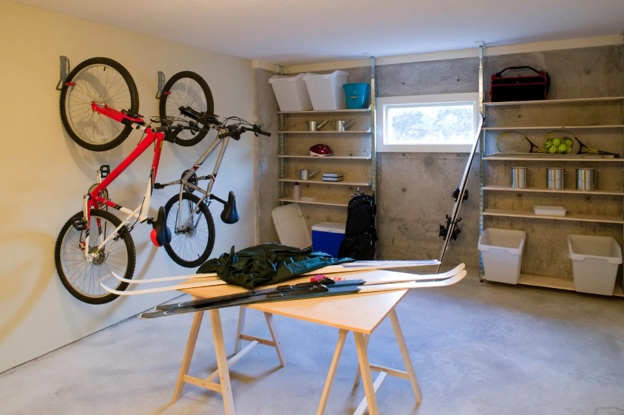 Small garage with two bikes hanging from the wall, a center table with skis, and organized shelves.