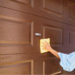 Woman in a blue shirt using a yellow rag to clean the outside of a garage door.