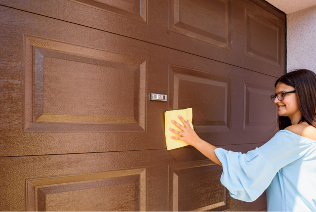 Woman in a blue shirt using a yellow rag to clean the outside of a garage door.